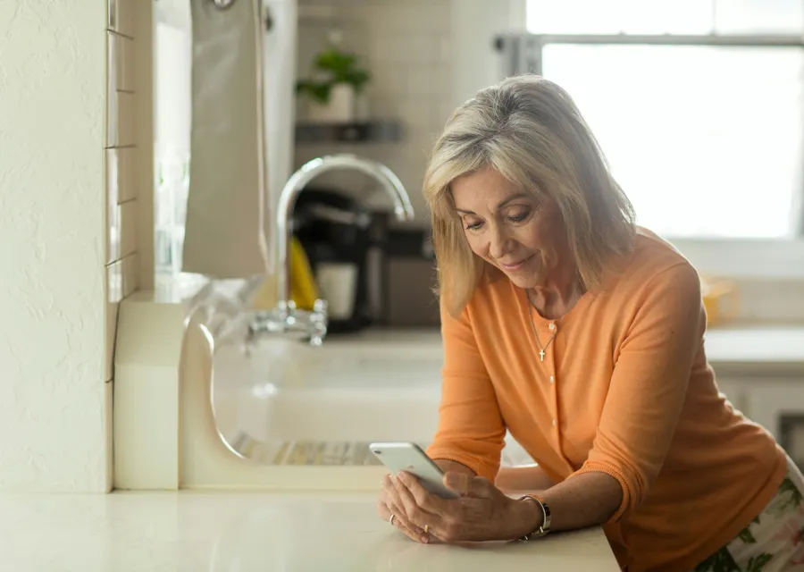 Femme souriante qui ouvre son dossier de vente sur son téléphone, dans sa cuisine